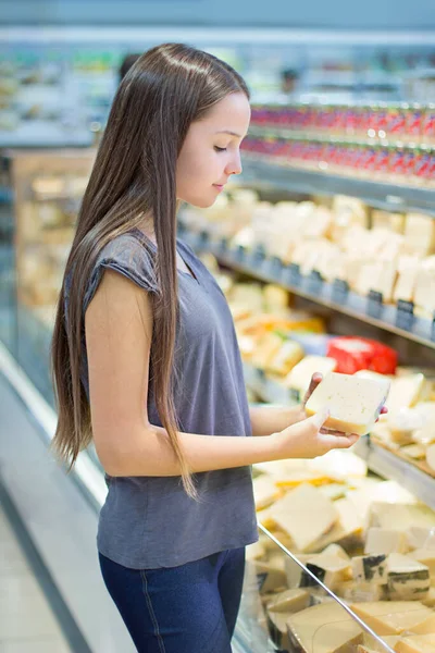 Teen girl shopping in supermarket, at dairy section. Reading product information, choosing daily product. Concept of conscious choice of healthy food by teenager\'s.