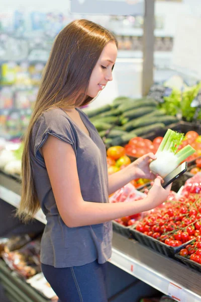 Teen girl shopping in supermarket, reading product information, choosing daily product. Concept of conscious choice of healthy food by teenager\'s.