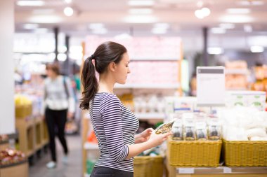 Kadın süpermarkette günlük ürünleri seçiyor. Ürün bilgileri okunuyor. Bilinçli sağlıklı yiyecek seçimi kavramı. 