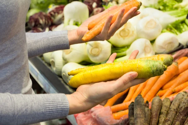 Female hand choosing carrots in supermarket. Concept of healthy food, bio, vegetarian, diet.