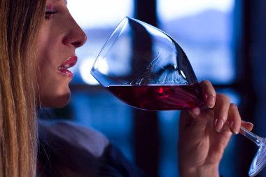 Akşam gün batımında evde bir bardak kırmızı şarap içen genç bir kadın.