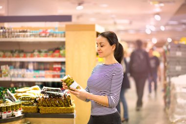 Kadın süpermarkette günlük ürünleri seçiyor. Ürün bilgileri okunuyor. Biyolojik ve sağlıklı besin seçimi kavramı.