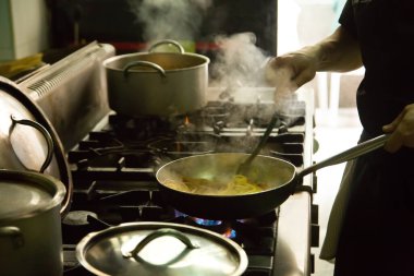 Mutfaktaki ocakta çelik tencereyle yemek pişiren adam.