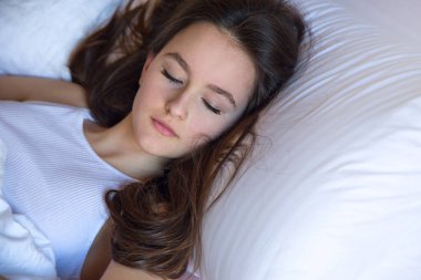 Uyuyan genç kız, sabahları rahat bir yatakta sağlıklı bir şekerlemenin tadını çıkarıyor. Milenyum kızı, yumuşak yastıkta dinleniyor ve beyaz pamuklu rahat bir yatak giyiyor..