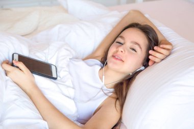 Uyandığında cep telefonu kullanan genç kız, sabah uyandığında cep telefonu kullanan kızın üzerinde mutlu hissediyor.