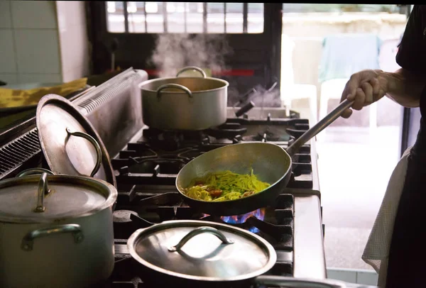 Hand man cooking with a steel pot on the stove in the kitchen