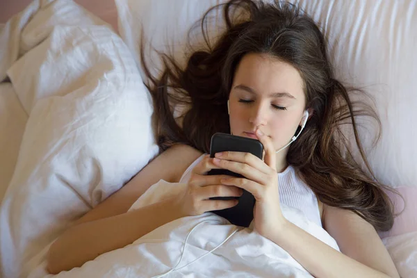 Teen girl using cell phone on waking feels good in the morning on the bed