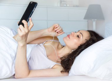 Uyandığında cep telefonu kullanan genç kız, sabah uyandığında cep telefonu kullanan kızın üzerinde mutlu hissediyor.