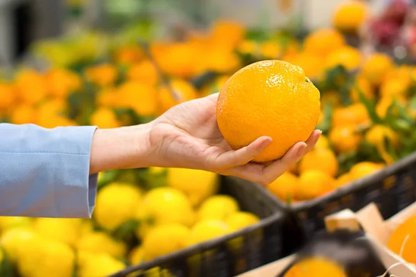 Woman's hand choosing orange at supermarket