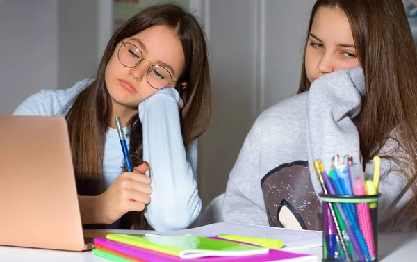 Two girls do homework with the help of the laptop. Too much information can bring fatigue and exhaustion. The concept of communication and navigation, the Internet, social network.