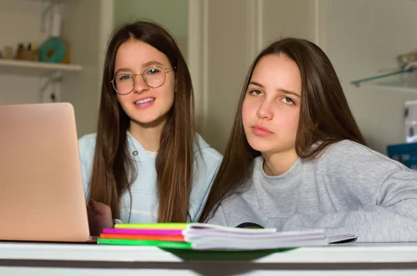 Two teen girls do homework with the help of the laptop. Too much information can bring fatigue and exhaustion. The concept of communication and navigation, the Internet, social network.
