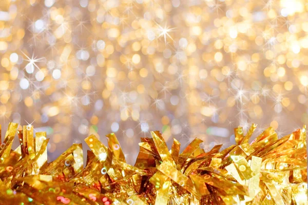 Nahaufnahme goldenes, glänzendes Lametta unten im Vordergrund auf goldenem Bokeh-Hintergrund mit Sternchen und Kopierraum. — Stockfoto