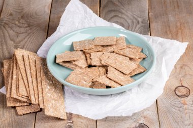 Yuvarlak tabakta ve ahşap masa üzerinde beyaz ambalaj kağıdı üzerinde Mısır havadar gevrek ekmekler. 