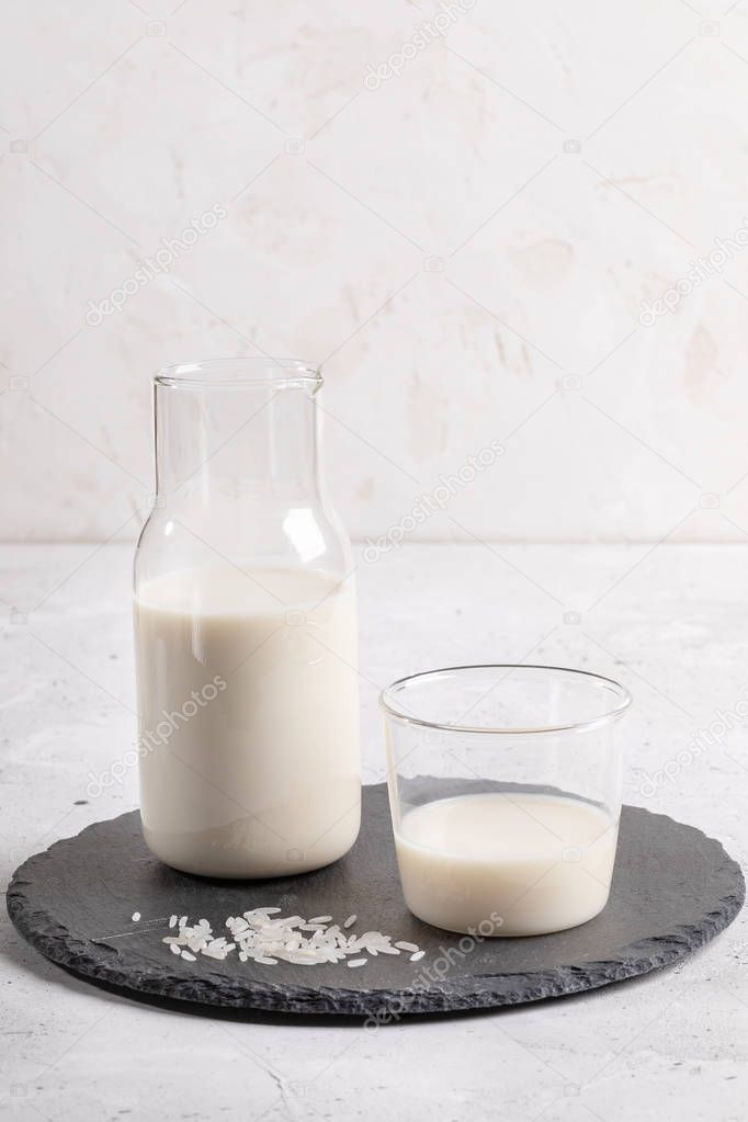 Drinking glass and glass bottle with healthy rice milk on round shale board on white background. 