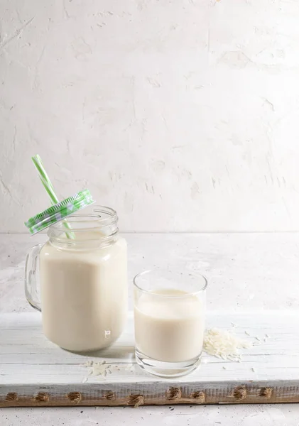 Copo de beber e caneca de pedreiro de vidro com leite de arroz saudável no tabuleiro de madeira no fundo branco . — Fotografia de Stock