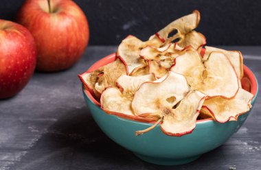 Turkuaz seramik kase de yakın çekim sağlıklı elma yongaları ve koyu gri arka plan üzerinde iki bütün elma.