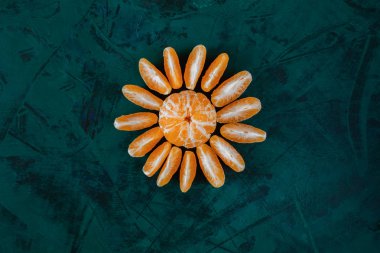 Parlak zümrüt yeşili arka plan merkezinde güneş veya çiçek gibi ortaya soyulmuş mandalina için üst görünüm.