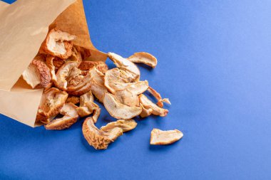 Mavi arka plan üzerinde kağıt torbadan dağıtılan kurutulmuş elma dilimleri. 