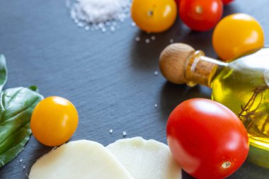 Kırmızı ve sarı domates, mozzarella peyniri, zeytinyağı ve yeşil Fesleğen koyu şist tahtası üzerinde daire içinde yatıyor.