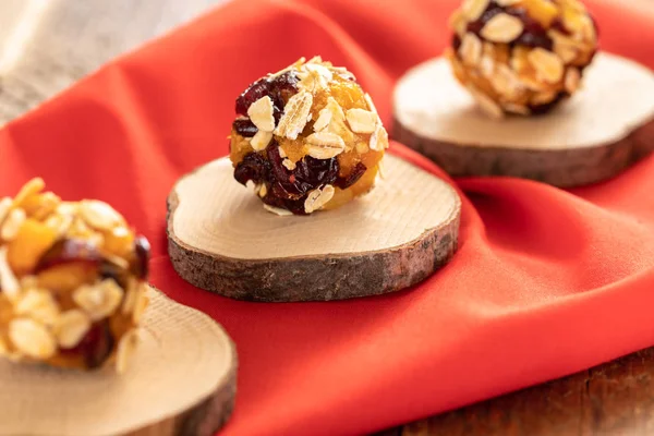 Three homemade energy ball are lying diagonally in row on wooden saw cut on red fabric.