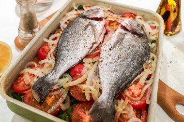 Balık, beyaz masada metal fırın tepsisinde sebze yastığı üzerinde pişirme için hazırlanan.