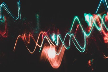 Siyah zeminüzerinde renkli kırmızı ve turkuaz parlayan dalgalı çizgiler. 