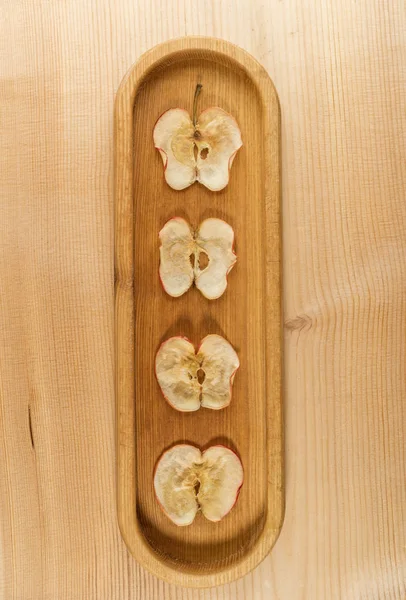 Four dried apple slices on oblong wooden plate on natural wooden