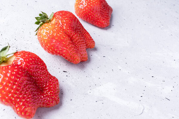 Three ugly red strawberries are lying diagonally on concrete background. 