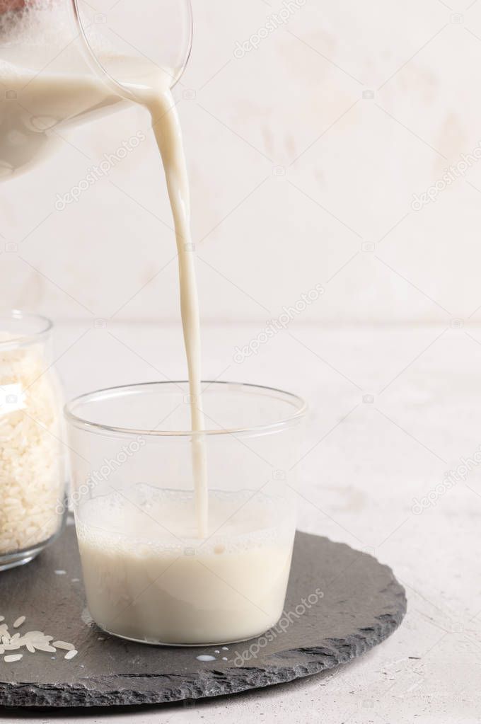 Healthy rice milk pouring from glass decanter into drinking glass on light background. 