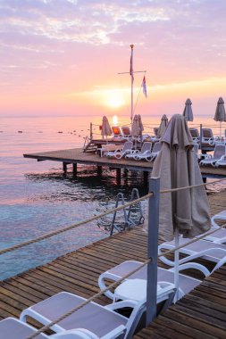 Boş şezlong ve şemsiyeler ile romantik gündoğumu gökyüzü, deniz ve platform görünümü.