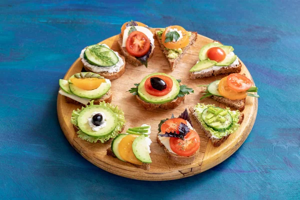 Round wooden kitchen cutting board with sandwiches with vegetables, cheese and herbs.