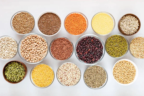 Top view to set of glass bowls with good for health cereals, beans and seeds on white background.