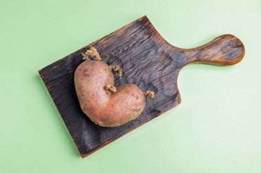 Yeşil arka planda yanmış ahşap mutfak tahtası üzerinde bir çirkin patates. 