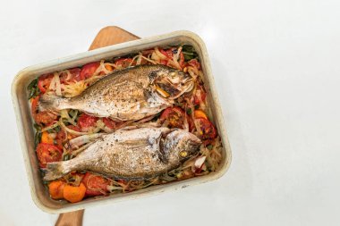 Balık, beyaz arka plan üzerinde metal fırın tepsisinde sebze yastığı üzerinde pişmiş.