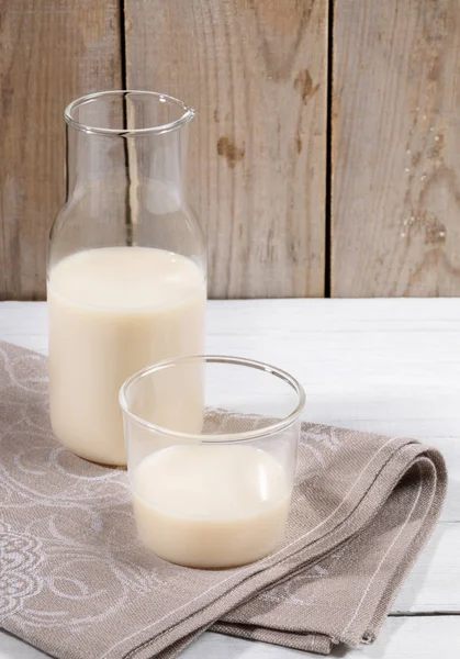 Oat milk in glass bottle and glass on linen napkin on old wooden background.