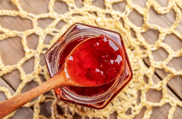 Wooden spoon full of  strawberry jam on yellow knitted napkin on