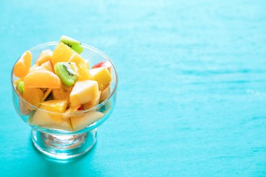Kopyalama alanı ile turkuaz arka plan üzerinde cam kase meyve salatası.
