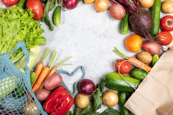 Fresh vegetables in net bag and in paper bag and laid out on concrete background with copy space.