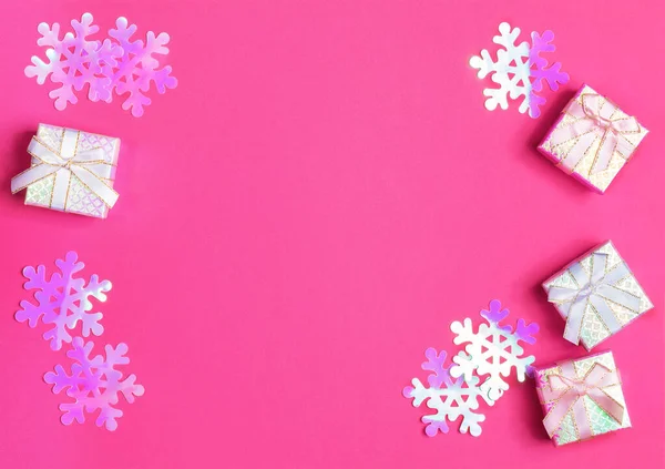 Cajas de regalo brillantes con cintas y lazos y copos de nieve púrpura de plástico iridiscente sobre fondo rosa. Diseño de Navidad . — Foto de Stock