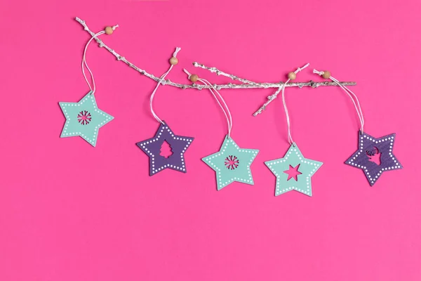 Juguetes de Navidad turquesa y púrpura pintado estrellas de madera sobre rama blanca sobre fondo rosa brillante . — Foto de Stock