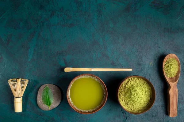 Set för matlagning matcha te: koppar med te och pulver, visp, skedar och blad som anges i rad på smaragd bakgrund. — Stockfoto