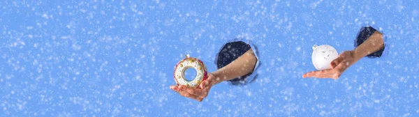 2人の女性の手は雪の装飾と青い紙の引き裂かれた穴を通してガラスクリスマスのおもちゃを伸ばす。コピースペース付きバナー. — ストック写真