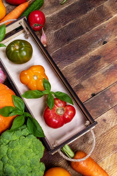 Невелика дерев'яна коробка з кольоровими свіжими стиглими фермами помідорами та овочами на старому сільському столі з копією простору . — стокове фото