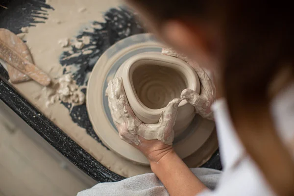A sculpts his hands with a clay cup on a potters wheel