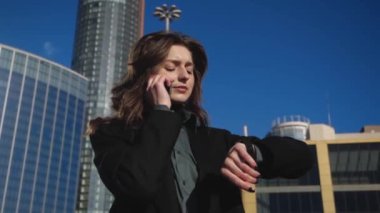 Genç iş kadını şehir manzarasının arka planında telefonla konuşuyor.