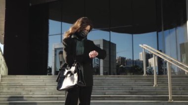 Koruyucu maskeli genç bir kız merdivenlerdeki saate bakıyor. 