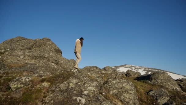 Una chica camina en el borde de un acantilado sobre el fondo de los picos de montaña — Vídeos de Stock