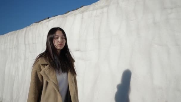 Zamyšlená krásná asijská žena kráčí po zasněžené zdi mžourající ze slunce — Stock video