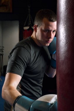 Spor salonunda kum torbasıyla boks yapan konsantre genç bir adam.