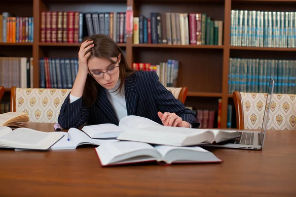 A student with glasses is trying to find information in textbooks. — Stock Photo, Image